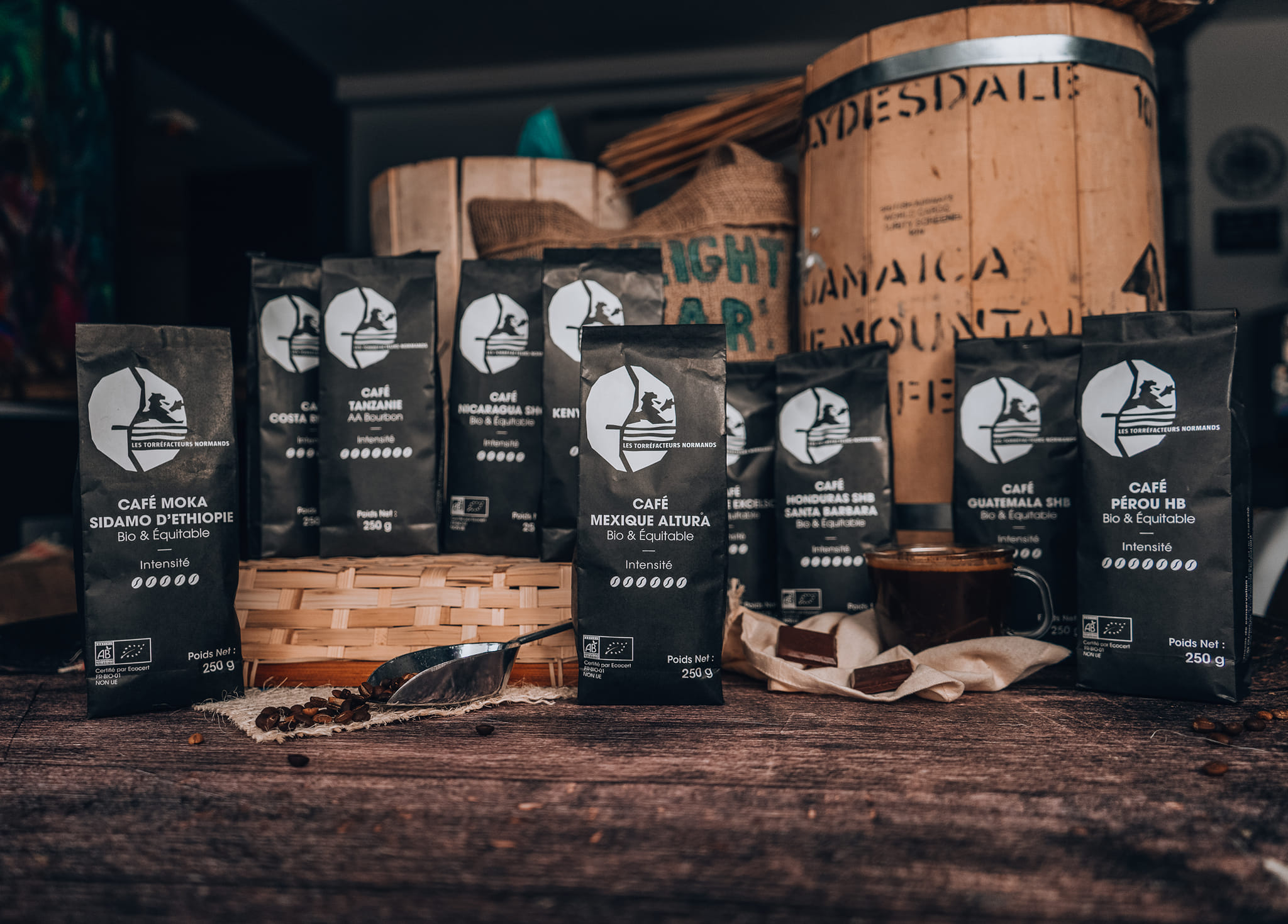 Une dizaine de paquets de café Les Torréfacteurs Français disposé devant des sacs de grain de café -  Torréfaction artisanale 